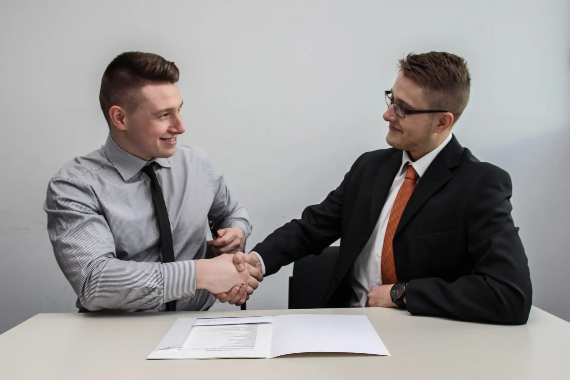 Two businessmen in business attire shaking hands over documents on a table.